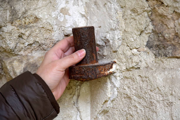 Female hand holds large antique loop embedded in stone wall. Old metal covered with rust. The ruins of an ancient synagogue. Old dilapidated masonry. Rashkov, Moldova. Close-up. Selective focus.