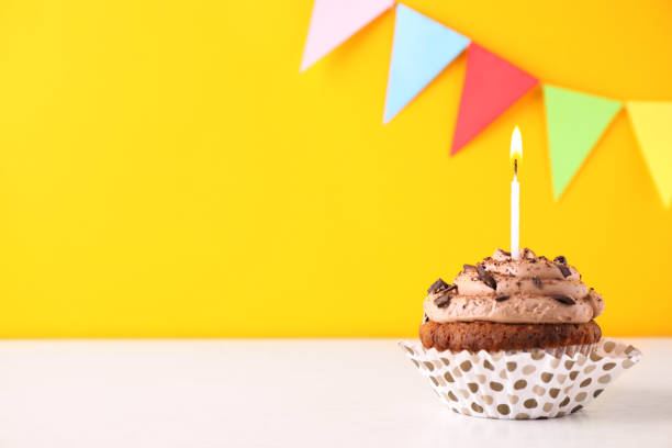 istock Chocolate cupcake with burning candle on white table against yellow background. Space for text 1391193718