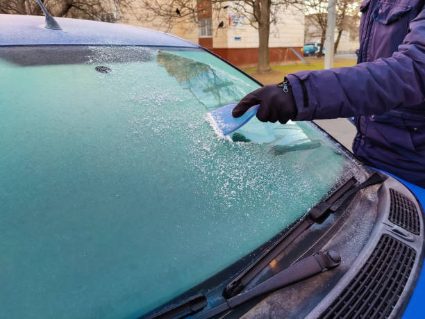 istock One man scrapes hoarfrost with plastic scraper from windshield of blue car. Male's gloved hand in cold. Building is in distance. Copy space. Selective focus. 1391193720