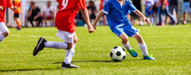 los niños juegan al fútbol. adolescentes jugando al fútbol en el campo deportivo. niños pateando juegos de fútbol al aire libre. jóvenes futbolistas masculinos que corren con uniformes deportivos rojos y azules - soccer ball youth soccer event soccer fotografías e imágenes de stock