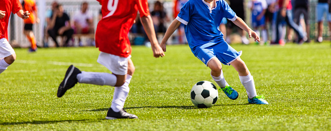 Smiling Mixed raced young sibling celebrating winning wearing blue soccer uniform sitting on grass.