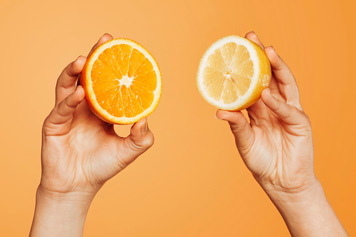 Close up of female hand holding a piece of orange and lemon over orange background at studio. Fresh juice fruit, summer concept.