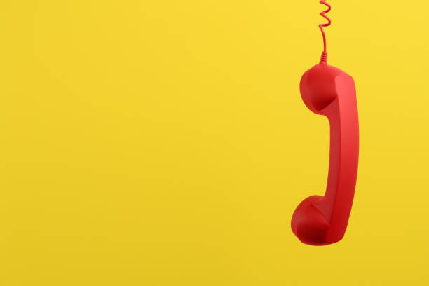istock Red corded telephone handset hanging on yellow background, space for text. Hotline concept 1391197128