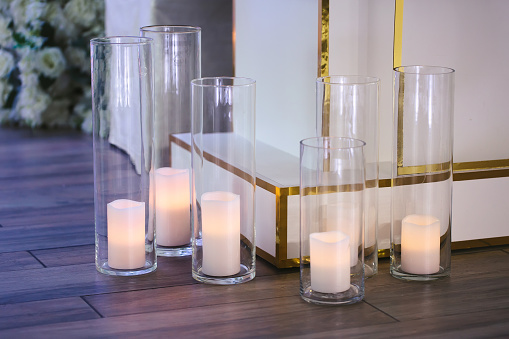 Burning white candles in glass vases on the floor. The cozy decor of the wedding ceremony.