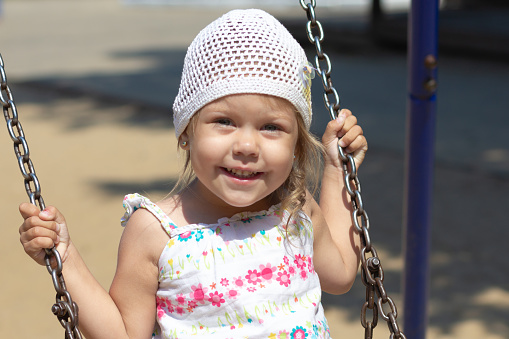 Smiling happy little girl swinging in the summer park