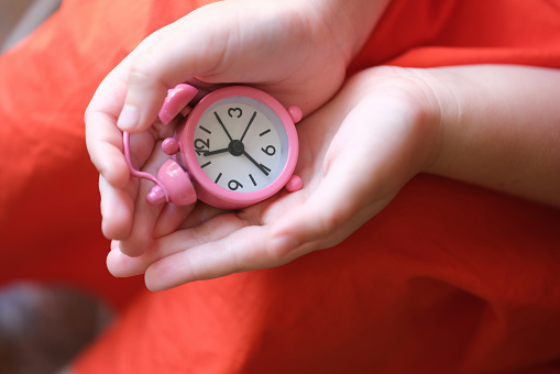 Pink clock compass in children hands closeup. Travel time control and childhood dreams