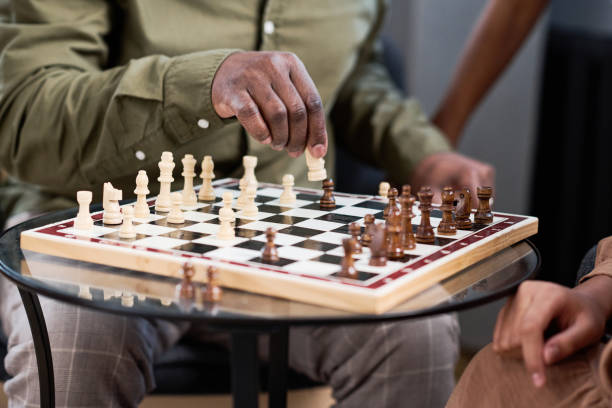 Hand of senior African American man putting white figure on chess board Hand of senior African American man putting white figure on chess board while playing leisure game with his two grandchildren senior chess stock pictures, royalty-free photos & images