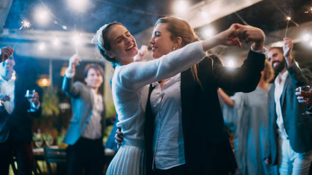 casal lésbico lindo celebra casamento em uma festa de recepção noturna com diversas amigas multiétnicas. recém-casados dançando e beijando em um restaurante. metas de relacionamento lgbtq. - homosexual couple lesbian wedding homosexual - fotografias e filmes do acervo