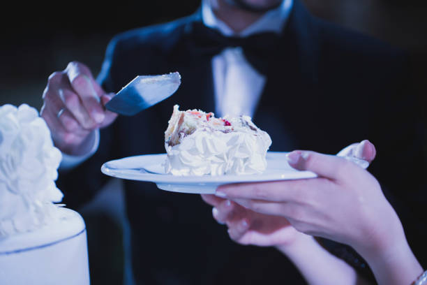 bride and groom tasting luxury wedding cake decorated with roses at reception, catering in restaurant