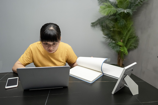 A young asian woman dressed in yellow sits in front of the office and works on a computer