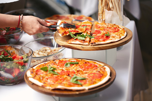 Stock photo showing close-up, elevated view of freshly made pizza dough base being covered with rich tomato sauce with a metal ladle in a swirling motion by hand of unrecognisable chef.