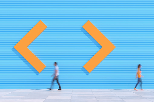 A man and woman walking towards the opposite directions of arrows on the pavement in front of a colored wall, persons blurred, Copy space background. 3D - computer-generated image
