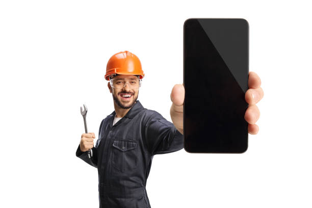 worker with an orange helmet holding a wrench and showing a smartphone - manual worker portrait helmet technology imagens e fotografias de stock
