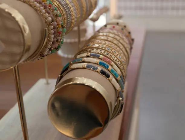 Glamorous and elegant bracelets or bangles in different colours. Gold-plated costume jewellery on display in a women's accessories shop. Exhibition of handmade costume jewellery.