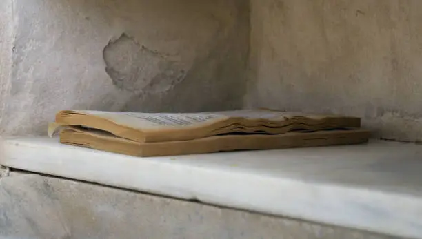 Photo of Broken and wet book abandoned on a marble shelf. Old book in poor condition abandoned on a shelf in the street.