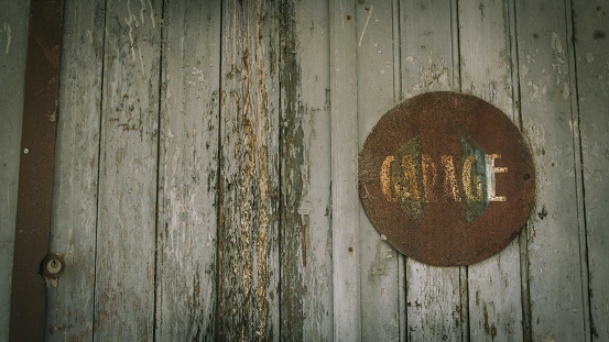 Uzès, France - June 18, 2014: A close-up of an old wooden door, which has a rusty 'garage' sign. Both show signs of wear and tear.