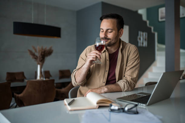 joven feliz disfrutando del vino mientras se toma un descanso del trabajo en casa. - glass drink alcohol red fotografías e imágenes de stock