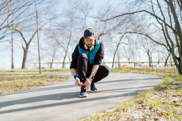 アスリートはジョギングの前にスポーツシューズを縛ります。都市公園の路上を走る男。春の朝はマラソンのトレーニングを外で過ごした - marathon sport sports training city street ストックフォトと画像