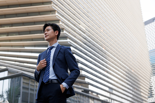 A young asian businessman about 30 years old stood on the street of the business district, wearing a blue suit. Show a sense of confidence.