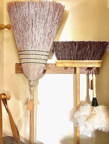Vertical still life of wall hanging rack rail with sweeping brooms duster in neutral brown and beige tones