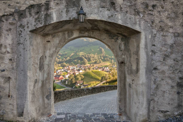 Liechtenstein - Balzers - The view through the stone gate under the antique lamp across the green valley towards the nice tiny town and hilly vineyard