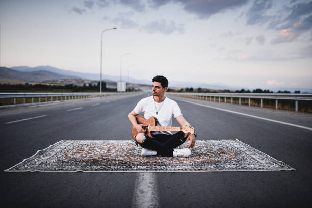 Guitarist Preparing For Show On Highway By Putting Down Carpet And Sitting On It