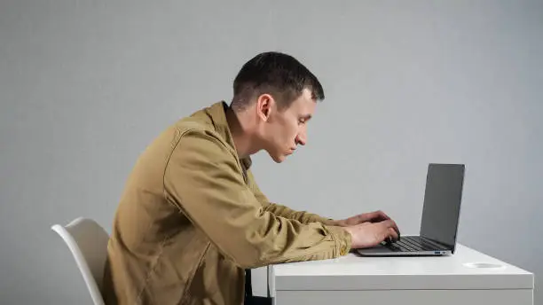 Photo of Man employee with crooked neck works on laptop in office