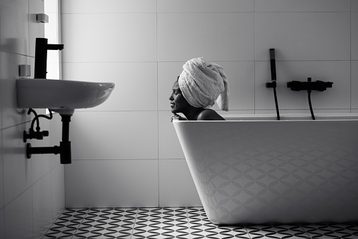 Portrait of Afro-American woman with a towel around her head relaxing in a bath. Female taking bath in the bathroom. Black and white image.