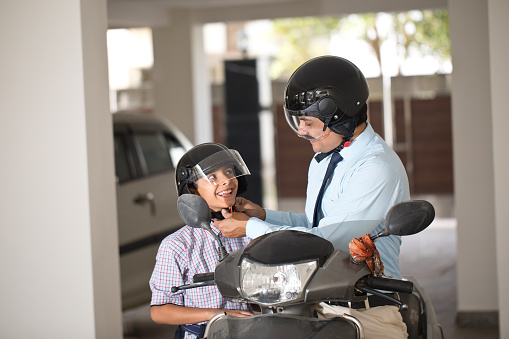 Father sitting on motorcycle and adjusting helmet of his son before leaving for school and office