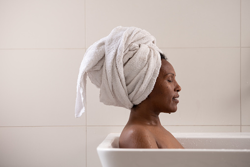 Portrait of a beautiful Ethiopian woman with a white towel on her head relaxing in a bathtub. Female taking bath in the bathroom.