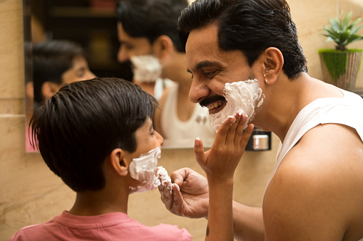 Father and son having fun applying shaving cream on face of each other in domestic bathroom