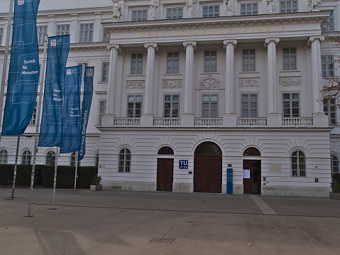 Vienna, Austria - 03-20-2022: Front view of the entrance of Vienna University of Technology (TU Wien, Austria) with blue colored logo and flags in an old building in the center of Vienna.