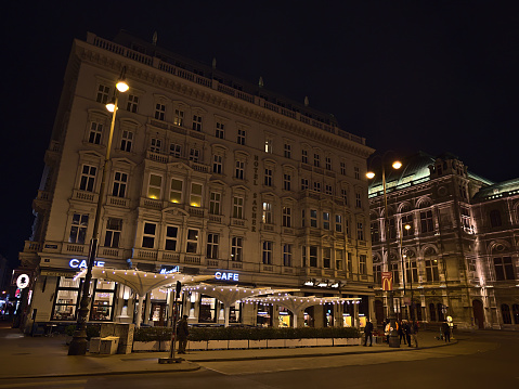 Vienna, Austria - 03-19-2022: Night view of famous luxury accomodation Hotel Sacher in the historic center of Vienna, Austria with illuminated facade, Cafe Mozart and Vienna State Opera.