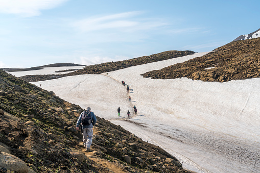 Senior men trekking from Highlands camping Kerlingarfjoll site to the Hveradalir geothermal area on Kerlingarfjoll mountain range, Iceland. In distance small group of tourists.