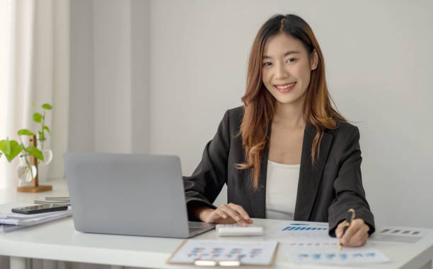 istock Charming Asian woman working at the office using a laptop Looking at the camera. 1391230781
