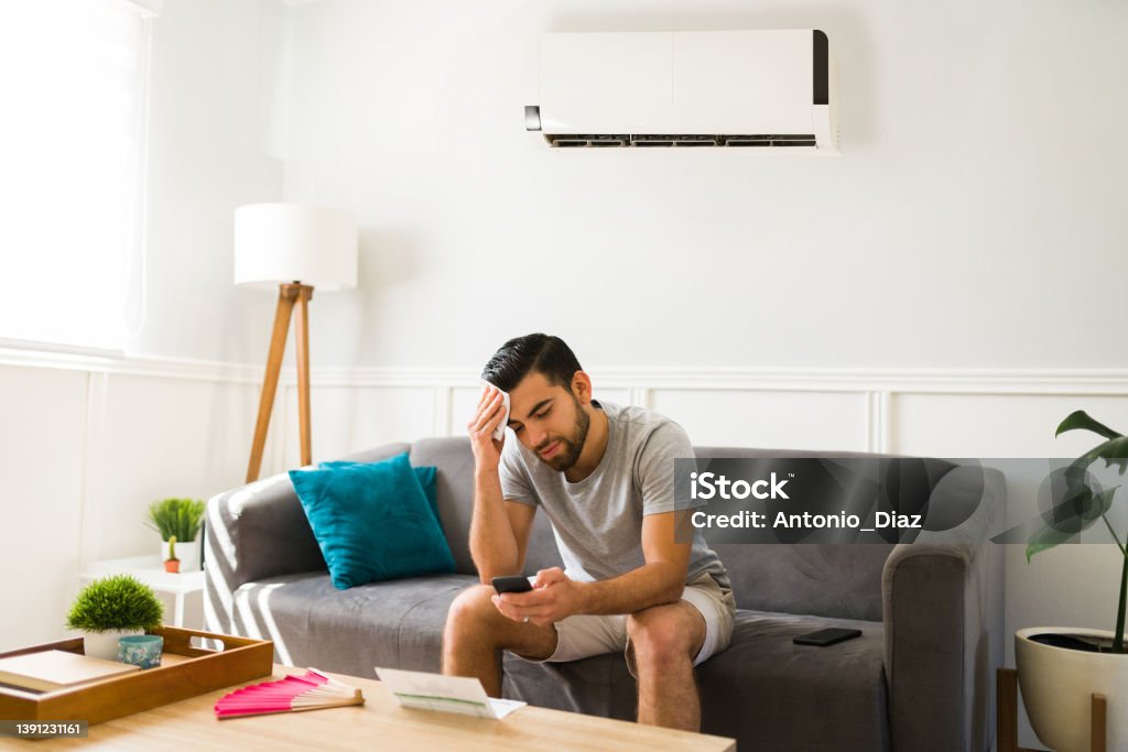 Sad man feeling hot without the air conditioner Upset man sweating during a heat wave in the summer while at home with a cold ac unit Sweat Stock Photo