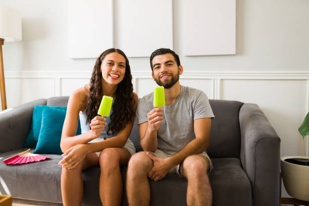 Hot summer. Smiling happy woman and man looking at the camera while holding an ice popsicle at home