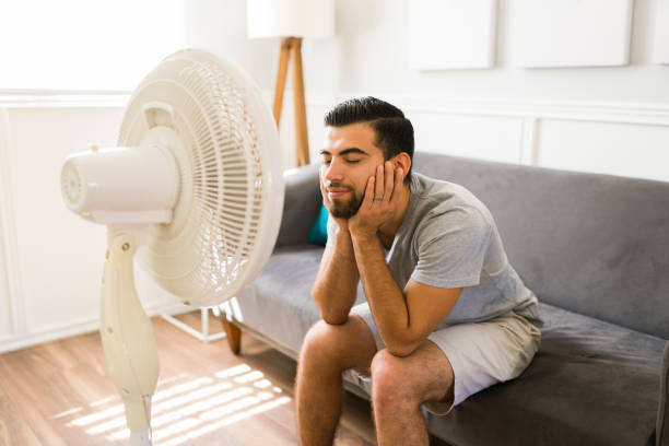 Relieved man enjoying the electric fan Happy young woman feeling better at home while relaxing in front of the electric fan during a bad heat wave electric fan stock pictures, royalty-free photos & images