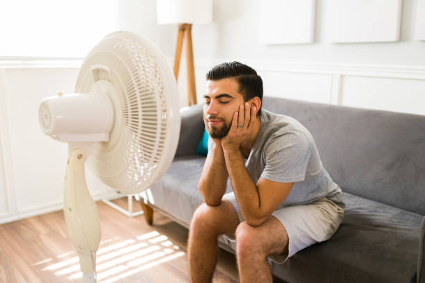 Relieved man enjoying the electric fan Happy young woman feeling better at home while relaxing in front of the electric fan during a bad heat wave young hot stock pictures, royalty-free photos & images
