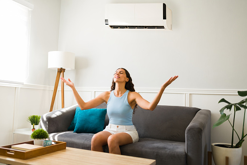Excited young woman using the best ac unit and enjoying the cold air flow at her home