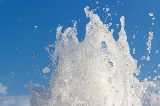 White foam and water bubbles from spraying fountain against blue sky. The upper part of the water column of the fountain