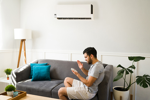 Frustrated young man feeling worried about the broken air conditioner and remote control