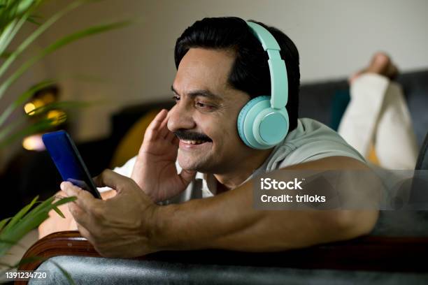 Man Listening Music Or Watching Video Using Mobile Phone And Headphones Stock Photo - Download Image Now