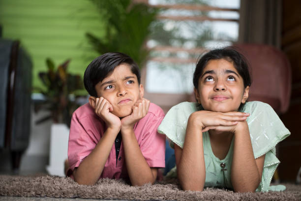 Brother and sister day dreaming while lying down on carpet in the living room