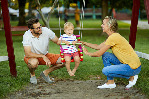 Young couple and their son having fun on swing at playground in park