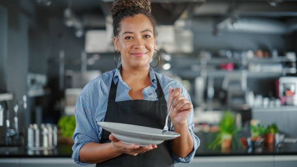 cocina del restaurante: retrato de la chef negra que prepara el plato, degusta la comida y la disfruta. cocina profesional deliciosa, auténtica, comida tradicional, utilizando ingredientes saludables para la receta de comida - tasting women eating expressing positivity fotografías e imágenes de stock