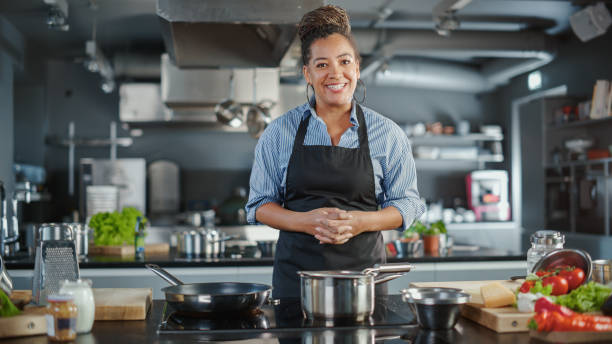 tv cooking show in restaurant kitchen: portrait of black female chef talks, teaches how to cook food. online courses, streaming service, learning video lectures. healthy dish recipe preparation - playback imagens e fotografias de stock
