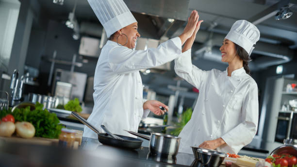 cucina del ristorante: ritratto di chef asiatici e neri che preparano il piatto, assaggiano il cibo, fanno high-five nella celebrazione di successo. due professionisti che cucinano piatti deliziosi, cibo autentico, pasti sani - food and drink healthy eating expertise professional occupation foto e immagini stock