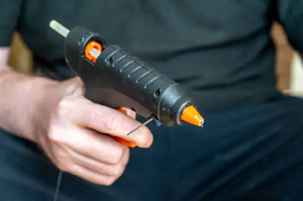 Photo of Close-up of a man holding a glue gun. A grown man with a hand tool.