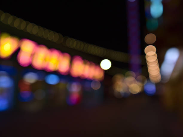 defocou (borrado) na noite de uma rua com lojas iluminadas em um parque de diversões popular perto de wiener prater na cidade de viena, áustria. imagem fora de foco. - wiener wurstelprater - fotografias e filmes do acervo